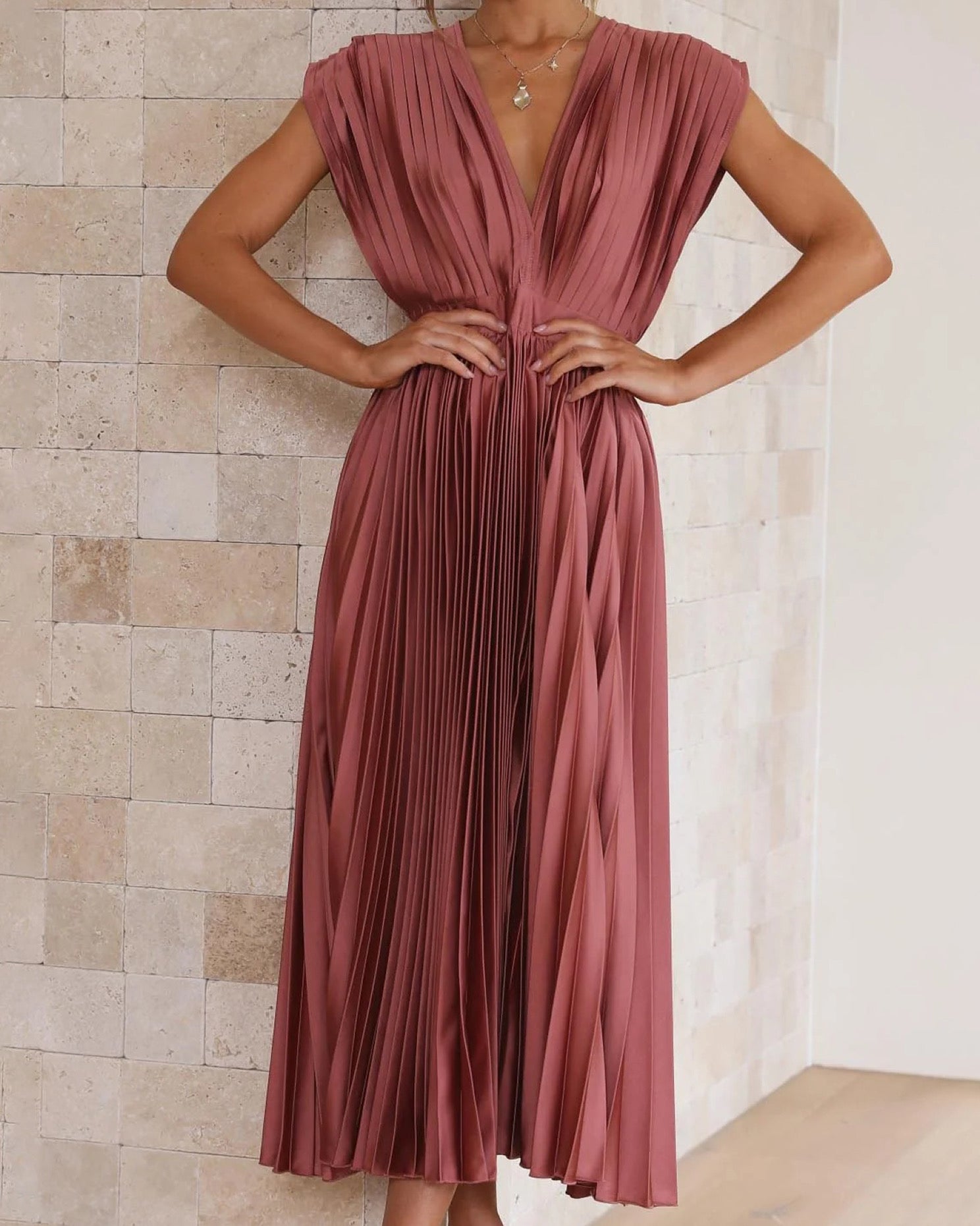 Woman wearing a pleated rust-colored dress against a tiled wall.