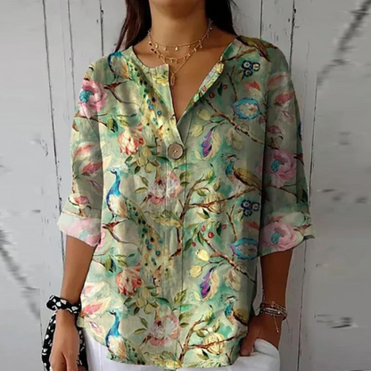 Woman wearing a floral blouse with birds and flowers against a wooden wall.