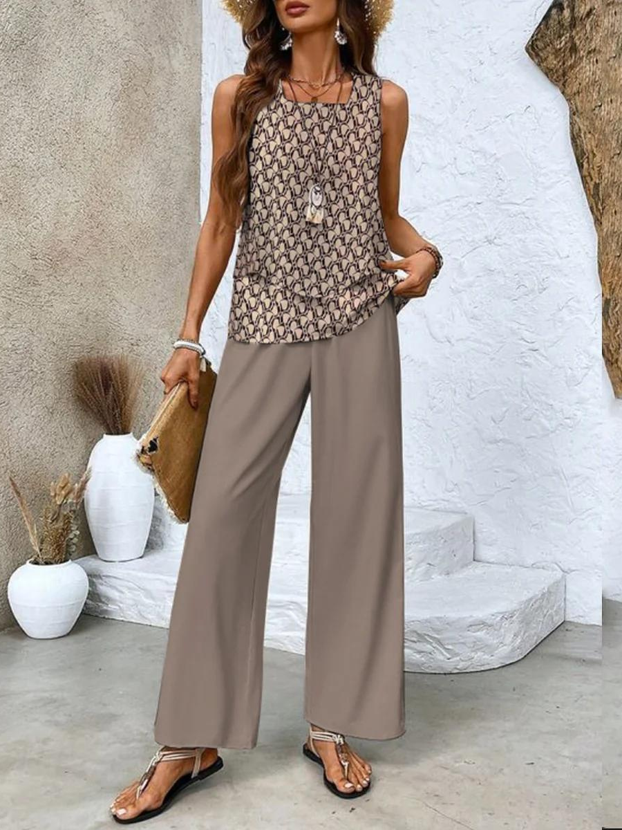 Woman wearing a patterned top and wide-leg pants standing against a textured wall.