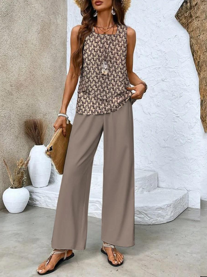 Woman wearing a patterned top and wide-leg pants standing against a textured wall.