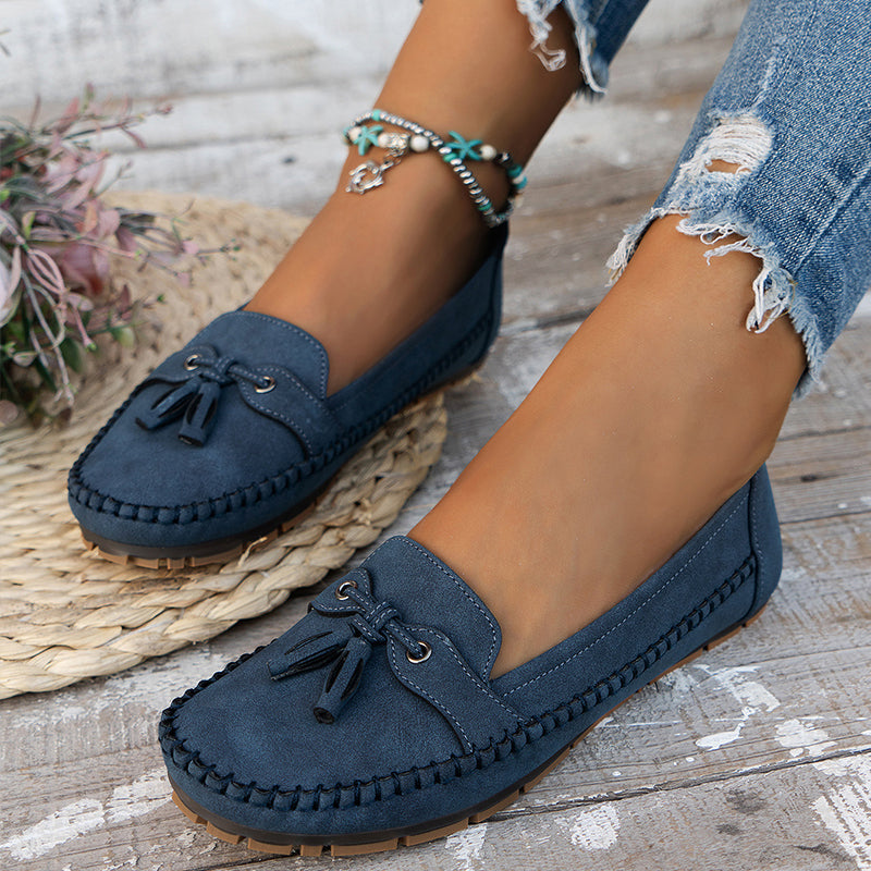 Navy blue loafers worn with ripped jeans on a wooden floor.