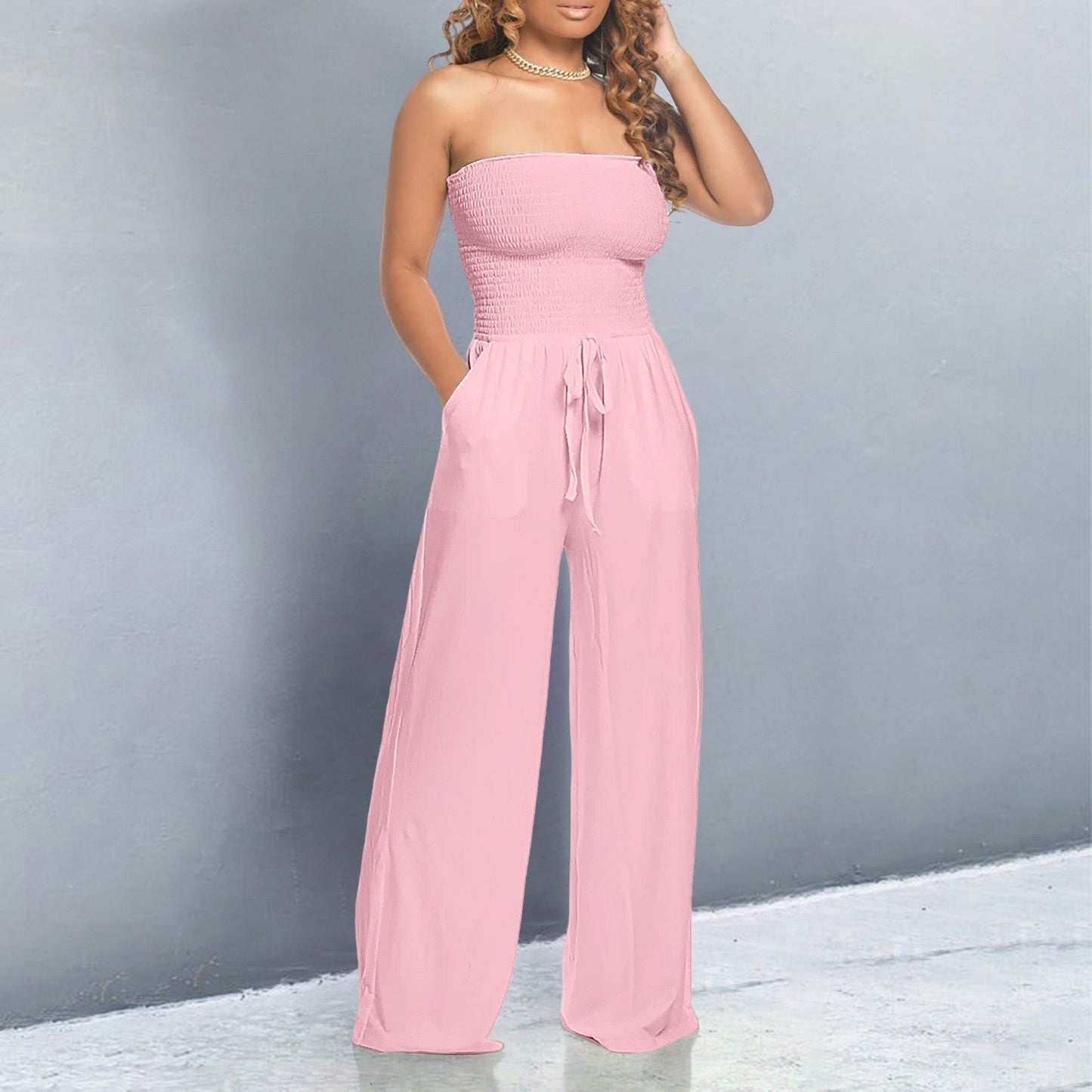 Woman wearing a pink strapless jumpsuit against a gray background