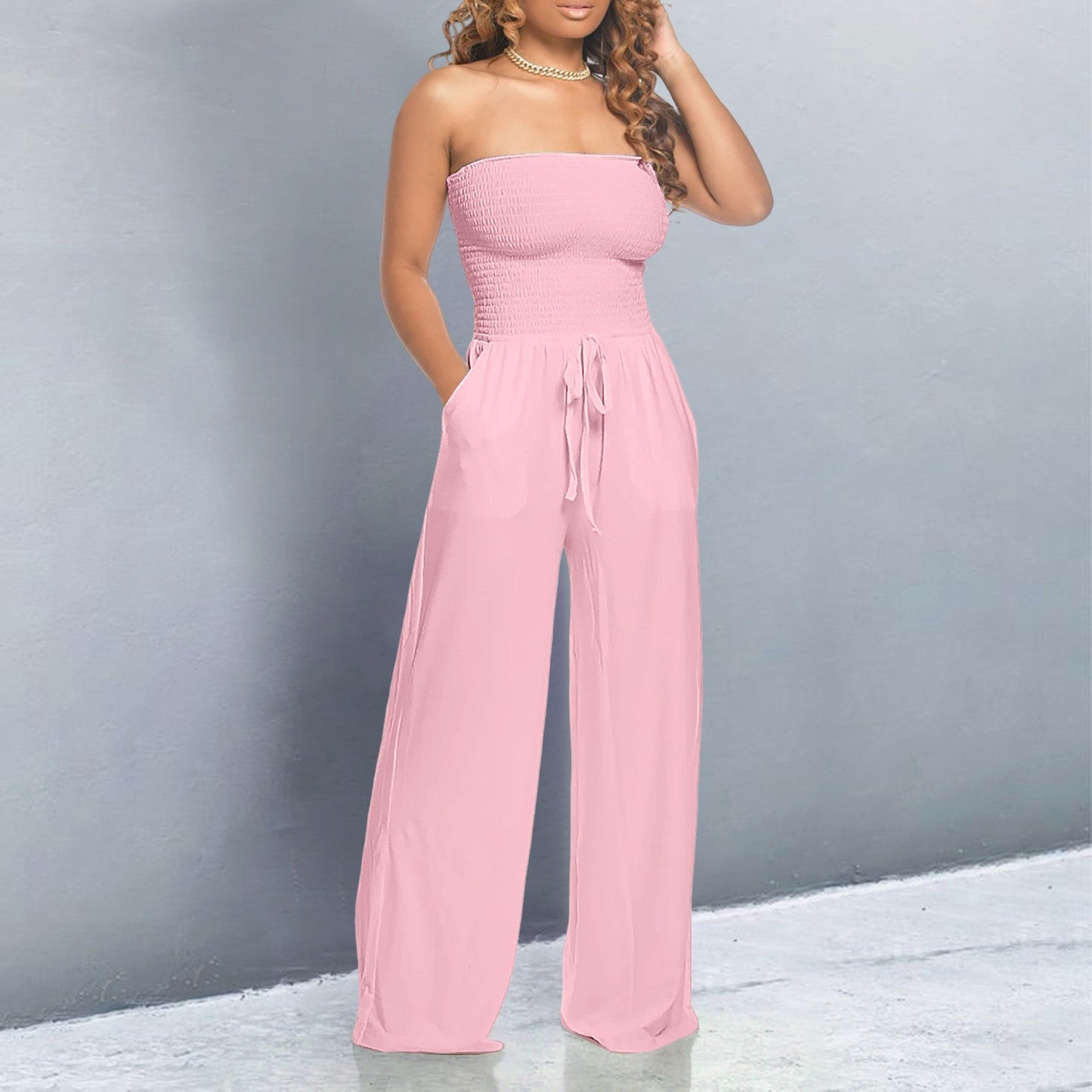 Woman wearing a pink strapless jumpsuit against a gray background