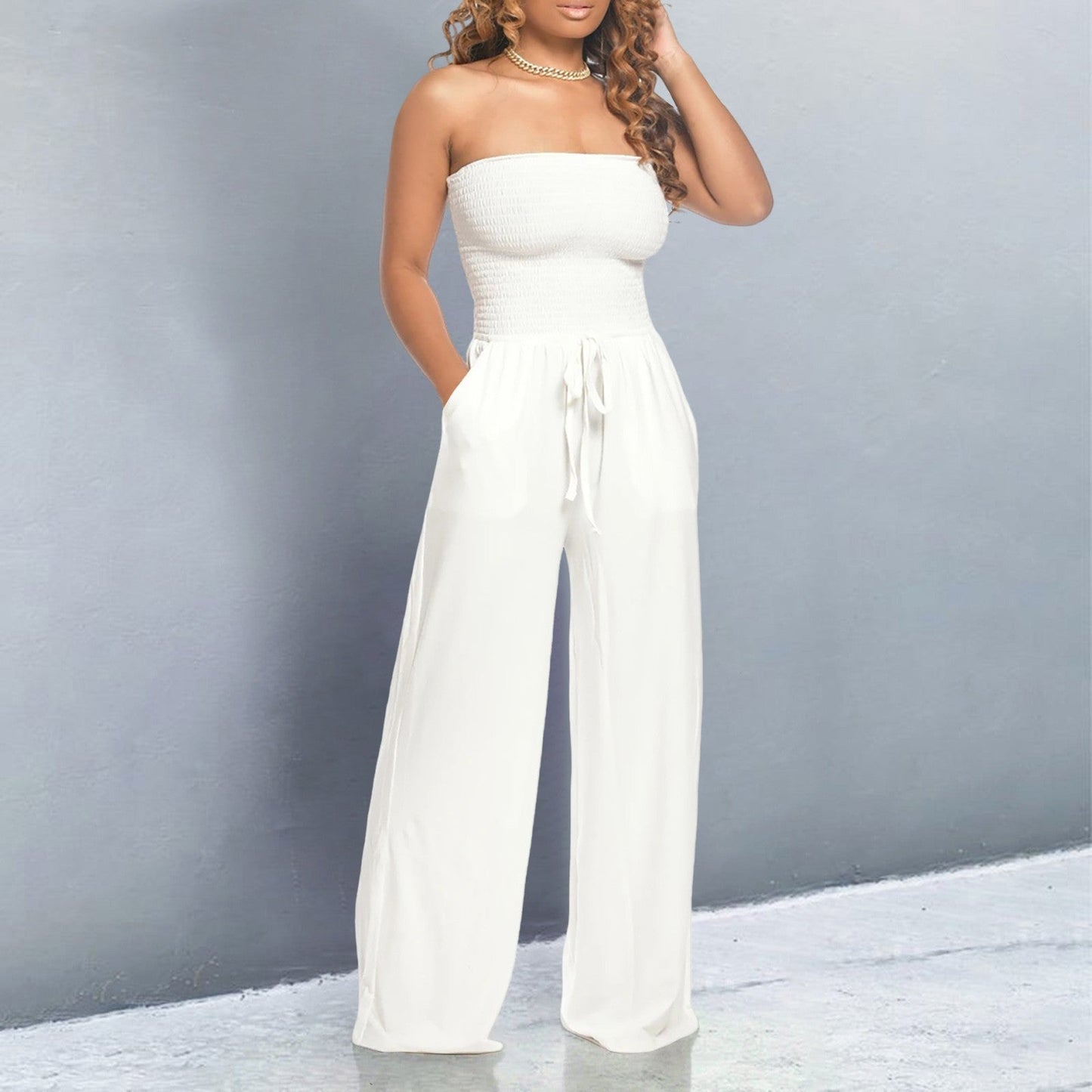 Woman wearing a white strapless jumpsuit against a gray background